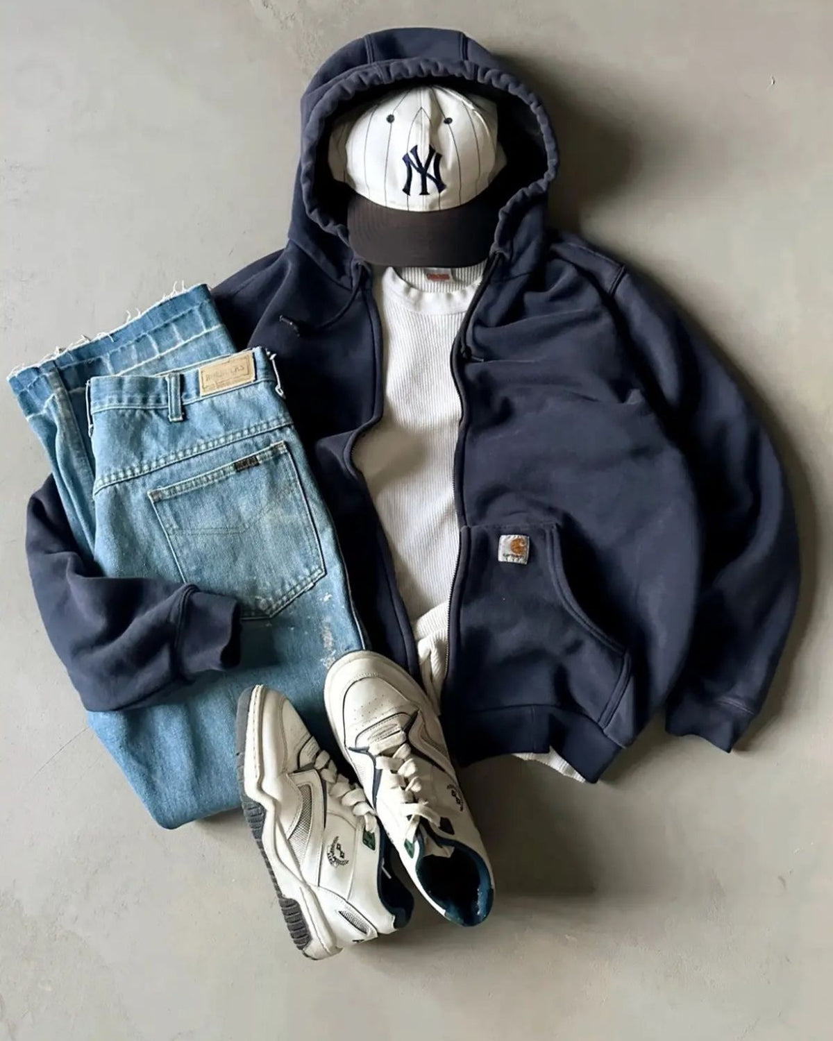 Outfit vintage steso a terra: felpa blu con cappuccio, maglietta color crema e jeans chiari